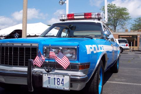 2001 Ford Crown Victoria - A blue police car, adorned with American flags, is parked outdoors under a bright sky.