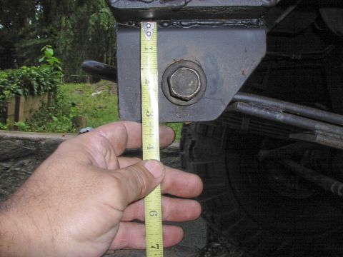 1986 Ford Bronco - A hand holds a tape measure against a vehicle's suspension component, with leaf springs in the background.