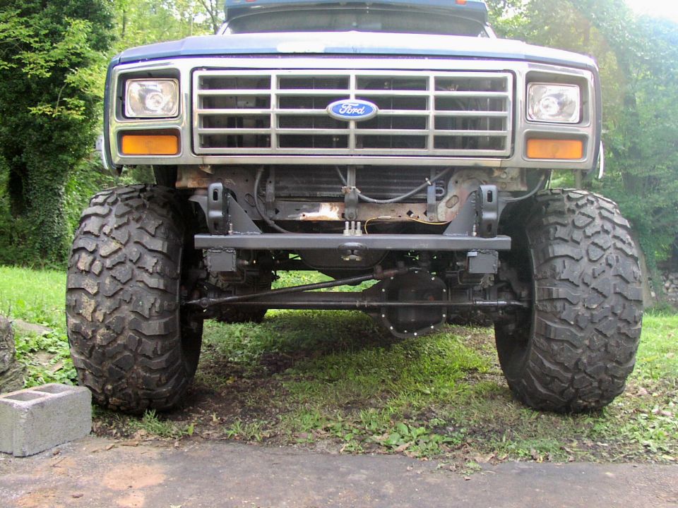 Front view of a lifted Ford truck with oversized tires and a chrome grille. The Ford logo is visible on the grille