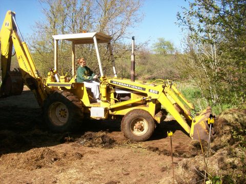 2000 Chevrolet Tahoe - A person operates a yellow International Harvester backhoe loader, moving dirt outdoors.