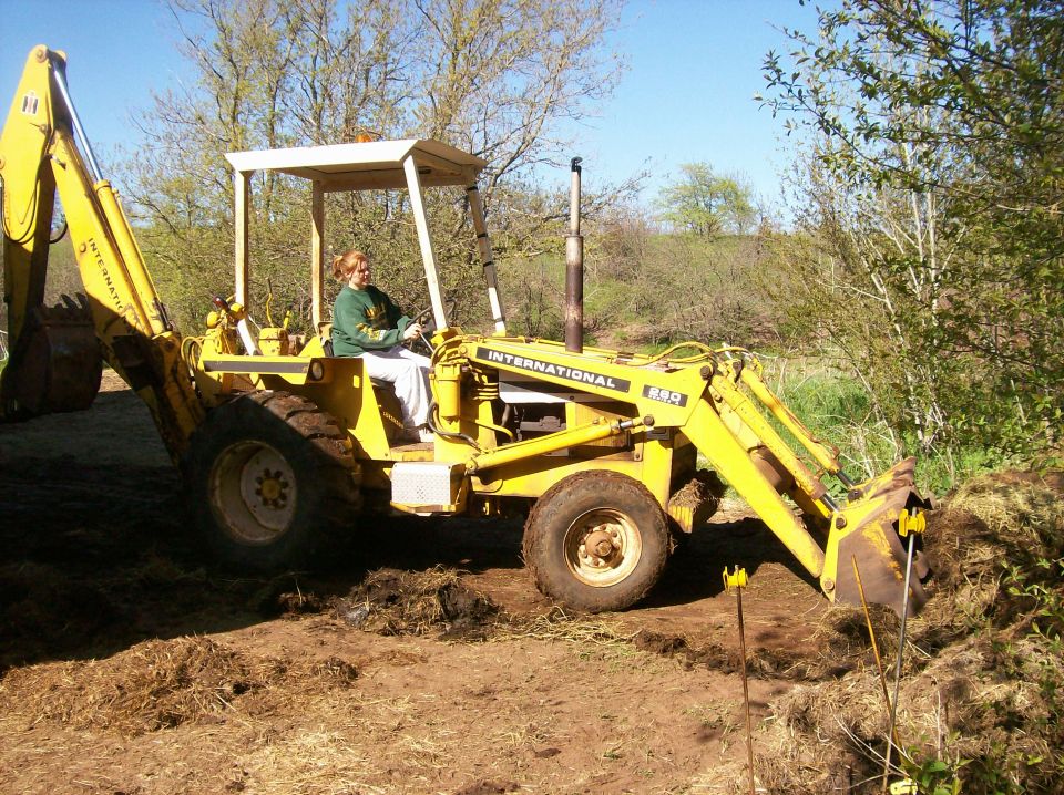 Yellow International Harvester backhoe loader with a person driving it, digging dirt
