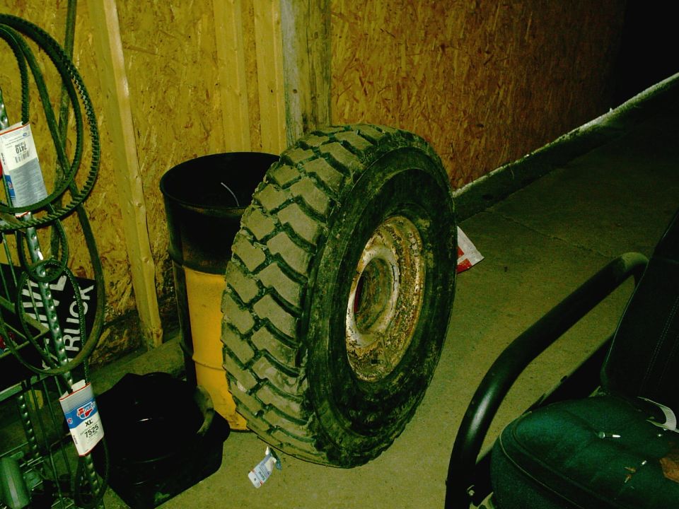 Tire and rim leaning against a wall, next to a yellow barrel