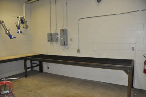 1996 Ford Bronco - A workshop scene long workbenches, fume extraction arms, and electrical panels mounted on a white cinder block wall.