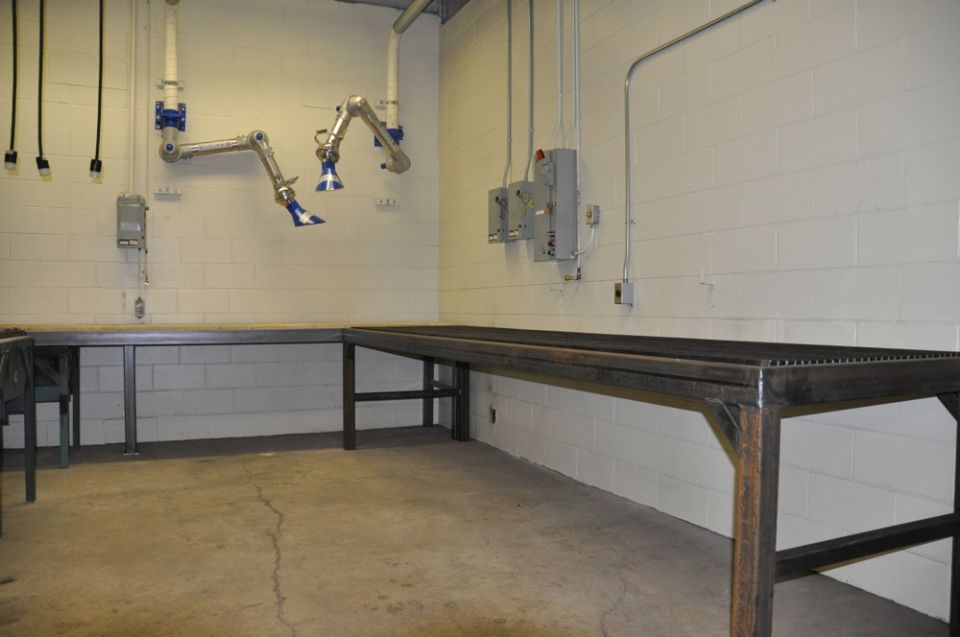 Two industrial workbenches and two articulated fume extractors mounted on a white brick wall