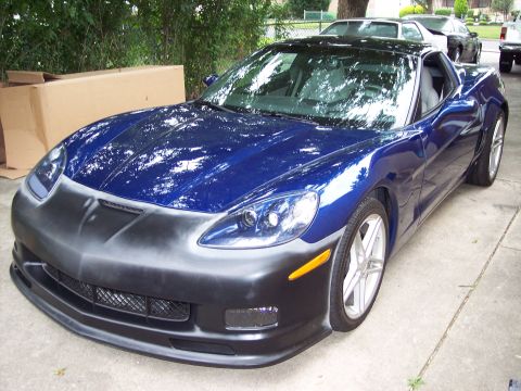 2006 Chevrolet Corvette - A blue Corvette is parked outside, showing its unpainted front bumper and other vehicles in the background.