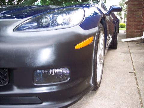 2006 Chevrolet Corvette - Front view of a blue Chevrolet Corvette with a black unpainted bumper section and visible headlight.