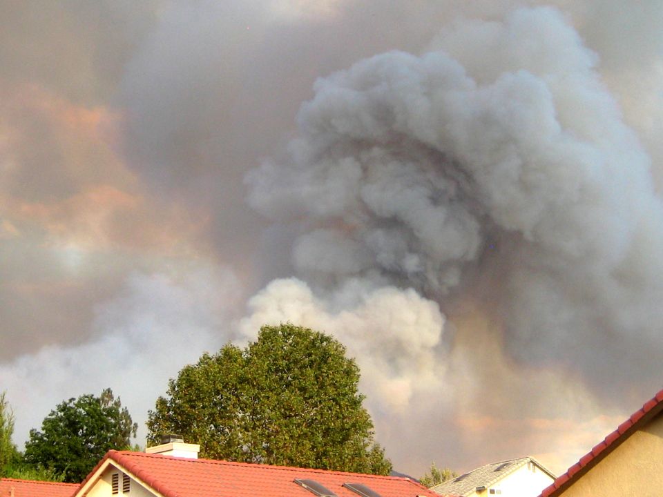 Big smoke cloud rising over trees and houses