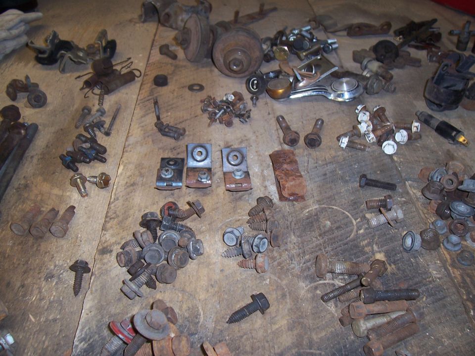 Pile of old bolts, screws, and metal brackets on a wooden surface