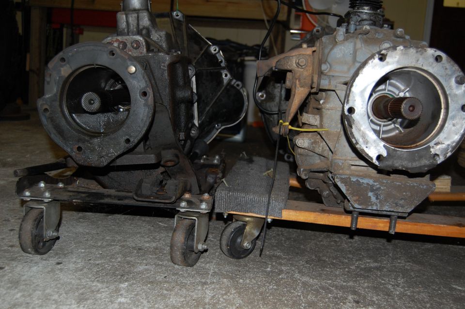 Two transmission assemblies on dollies, one black and one gray, with visible gears and mounting flanges
