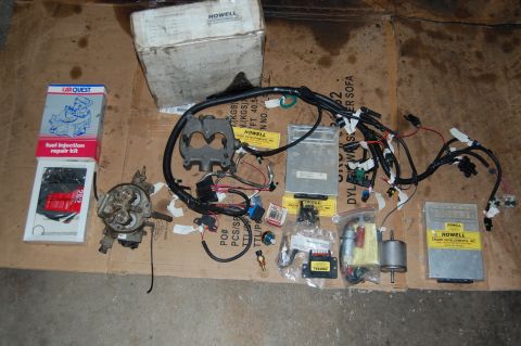 1994 Ford Bronco - Various fuel injection system components and wiring are laid out on a cardboard surface, including a repair kit, carburetor, and multiple H…