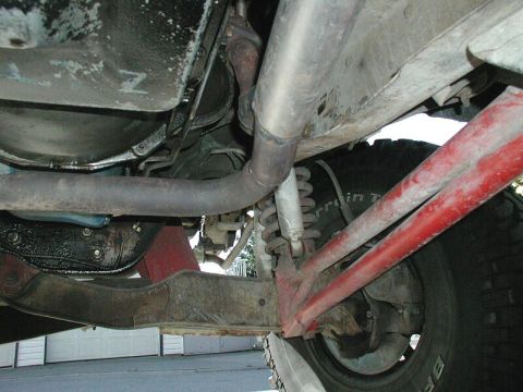 1985 Ford Bronco - Close-up of the exhaust system and suspension components, showing red painted control arms and a portion of the tire.