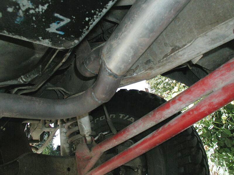 Undercarriage view showing exhaust pipes, muffler, and red frame bar over a tire