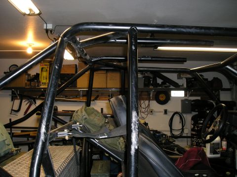 1986 Toyota Hilux - Vehicle interior a custom roll cage and aftermarket steering wheel, with storage shelves in the background.