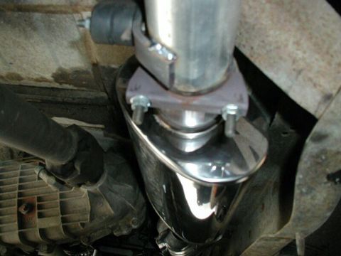 1985 Ford Bronco - Underside view of a shiny exhaust muffler attached to a vehicle's exhaust pipe.