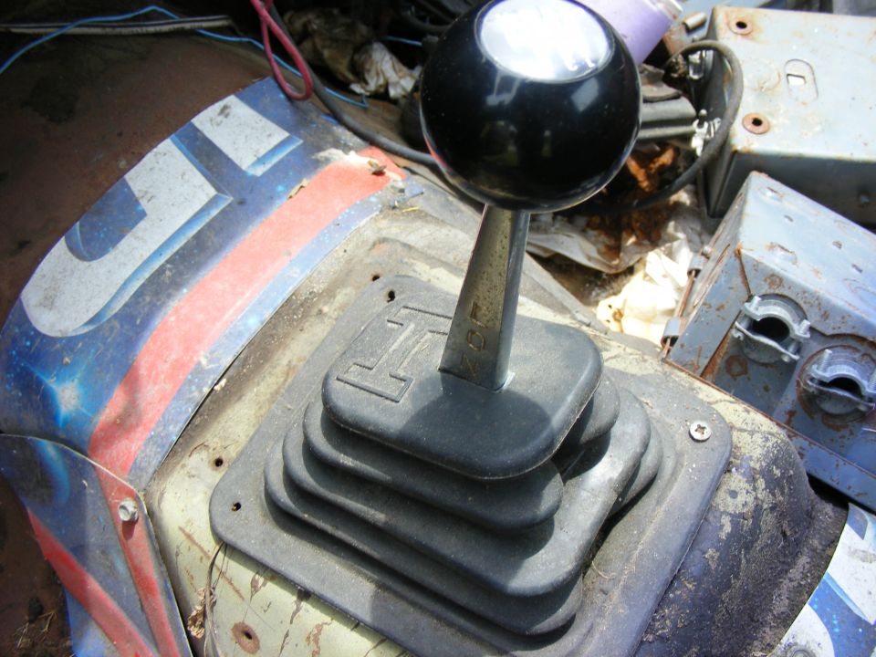 Black ball shift knob and rubber shifter boot on weathered, rusty vehicle floor panels