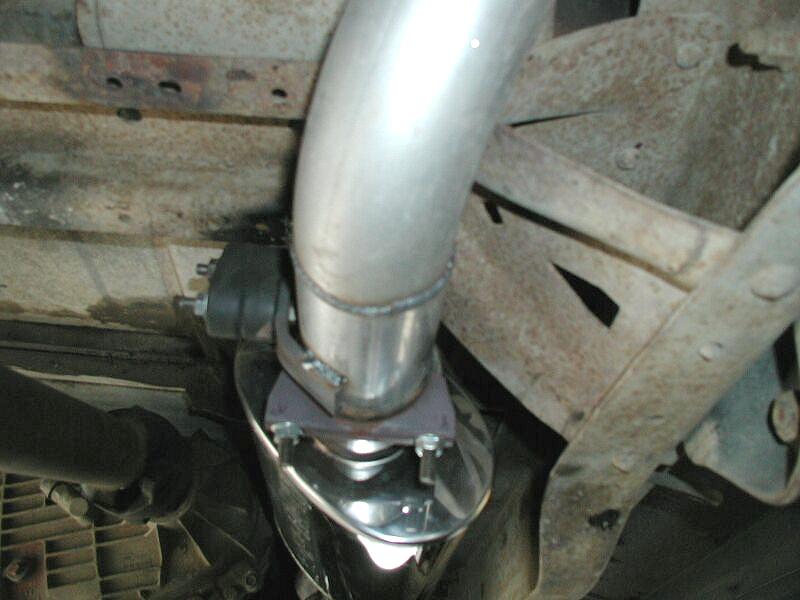 Polished stainless exhaust pipe and muffler bolted under a rusty vehicle chassis
