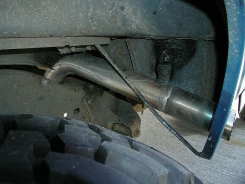 1985 Ford Bronco - A close-up view of the exhaust system and tire of a vehicle, revealing suspension details.