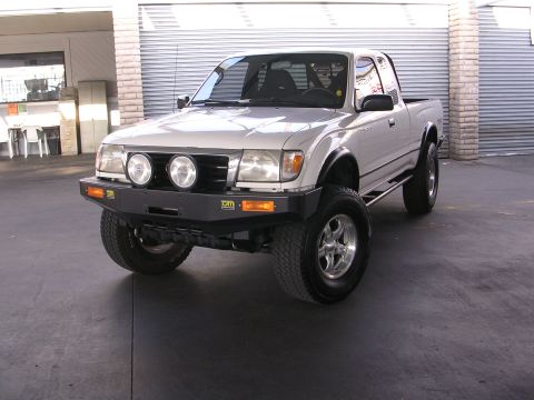 1999 Toyota Tacoma - Silver 1999 Toyota Tacoma pickup truck with aftermarket bumper and fog lights parked outside.