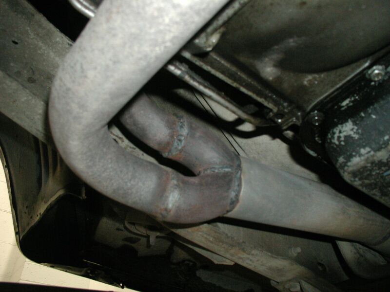 Underside exhaust Y-pipe junction with welds and surface rust near transmission