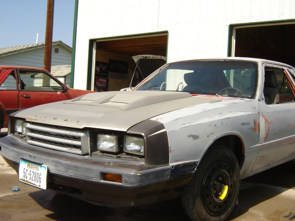 Primer-gray Mercury coupe in bare bodywork parked outside an open shop bay