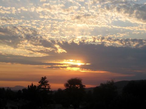 1996 Ford Bronco - The sun sets behind a layer of clouds, casting a warm glow over the sky and silhouetting trees and hills below.