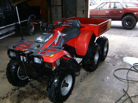 2000 Ford E350 - A red Polaris ATV with six wheels and a trailer is parked indoors next to a black truck and a maroon station wagon.