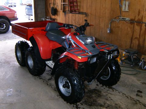 2000 Ford E350 - A red six-wheeled Polaris Big Boss ATV is parked inside a garage, with a red cargo bed attached.