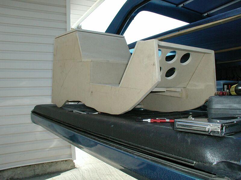 Unfinished MDF speaker/console box with three round cutouts on a blue tailgate
