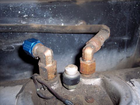 1981 Kenworth W900A - Detail of plumbing components, including a blue capped fitting and a sensor, against a dark, dusty background.