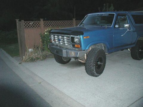 1985 Ford Bronco - Front view of a blue Ford Bronco, modified with an aftermarket bumper and off-road tires.