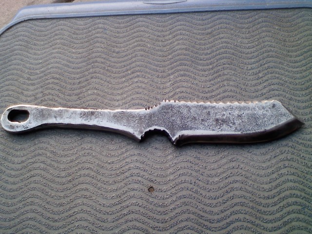 Hand-forged knife-shaped tool resting on a textured surface