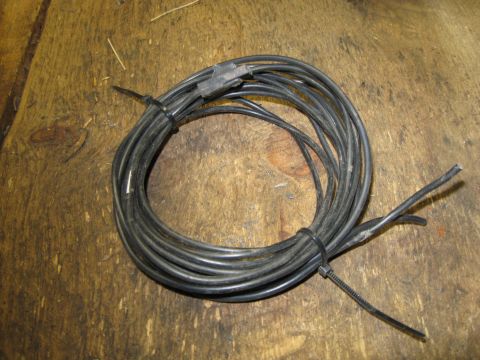 1979 Chevrolet Camaro - A coiled black wire with a connector and frayed ends lies on a wooden surface.