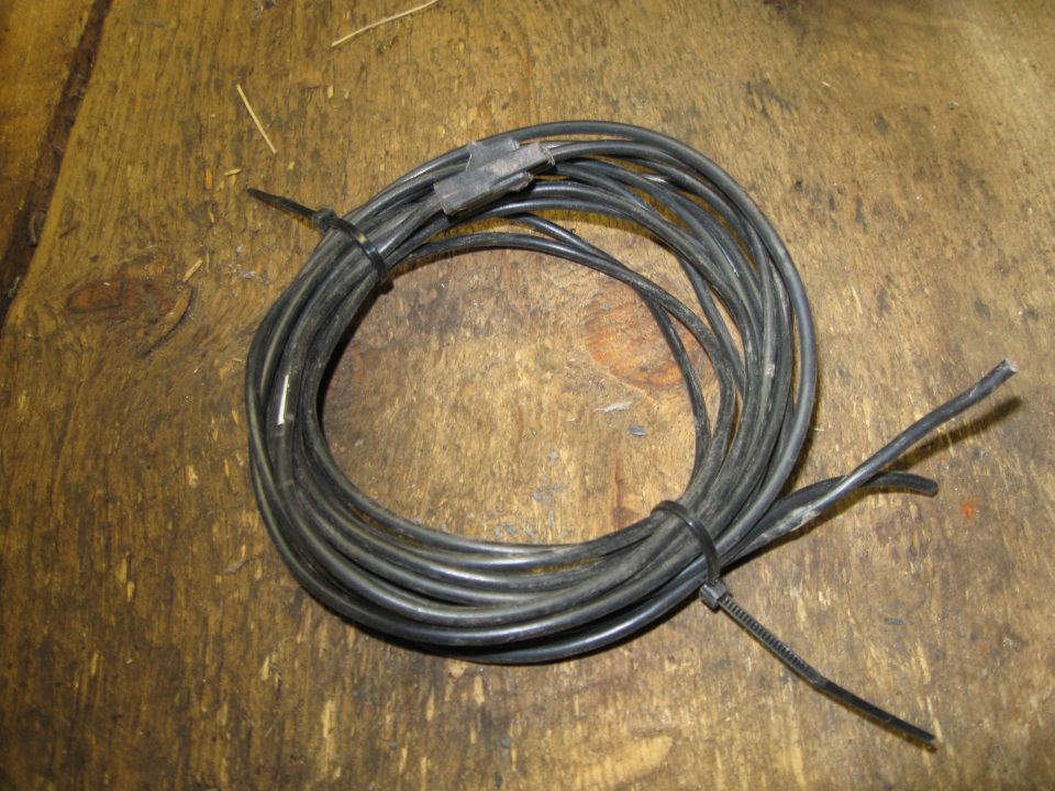 Coiled black wire with a plastic connector and frayed ends on a wooden surface
