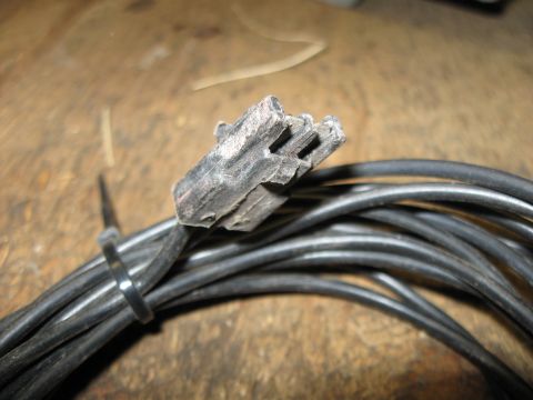 1979 Chevrolet Camaro - Close-up of a worn and damaged electrical connector attached to a bundle of black wires, resting on a wooden surface.