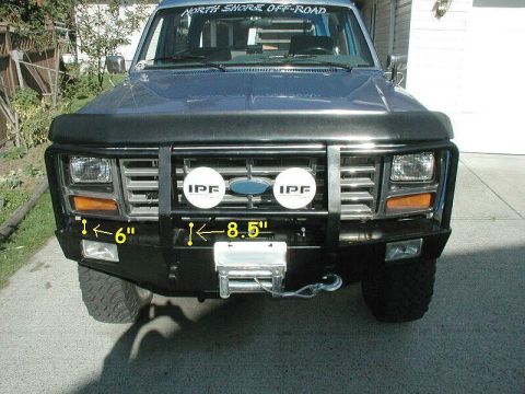 1985 Ford Bronco - Frontal view of a blue Ford Bronco with a custom bumper and auxiliary lights, showing its 1980s body style.