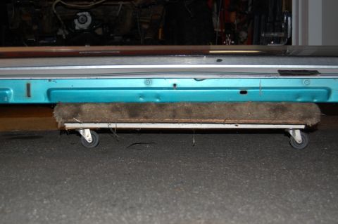 1994 Ford Bronco - A teal vehicle's lower body panel is shown resting on a wheeled dolly.