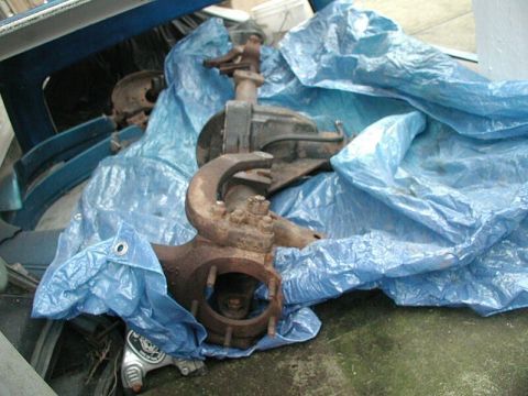 1985 Ford Bronco - A rusty front axle assembly is partially covered by a blue tarp, suggesting it is a spare part.