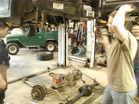 1985 Ford Bronco - A green Toyota Land Cruiser FJ40 is being worked on in a garage, with its drivetrain disassembled on the floor.