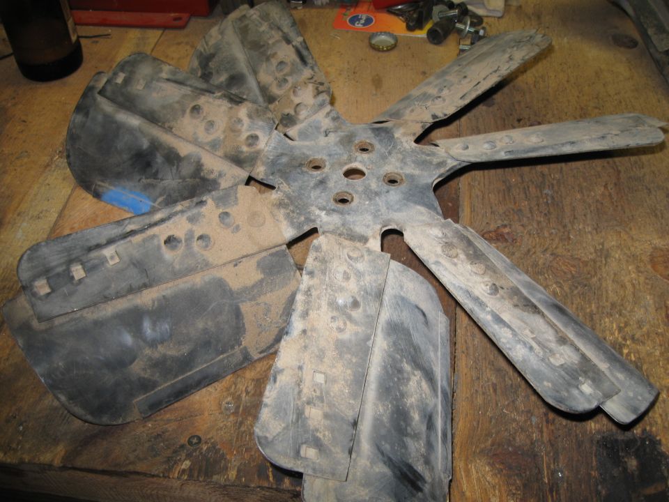 Radiator fan blade with six blades, metal hub, resting on a wooden surface