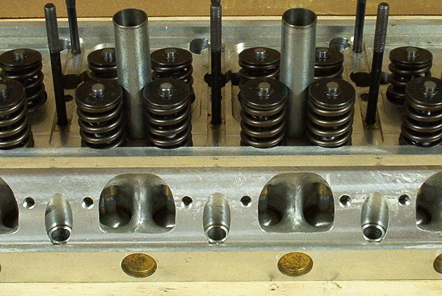 Engine cylinder head with visible valves, springs, and ports. Supermotors.net logo at bottom right