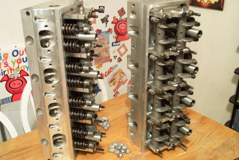 1972 Ford Ranchero - A pair of aluminum engine cylinder heads are displayed on a wooden surface, with various engine components scattered nearby.