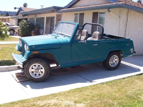 1970 Jeep Jeepster - This 1970 Jeep Jeepster convertible, seen in a driveway, features a teal exterior and a prominent roll bar.