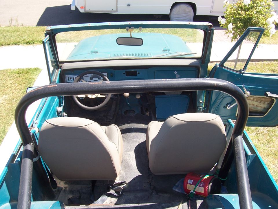 Interior of a teal Jeep with tan seats, roll bar, and dashboard visible. Doors are open
