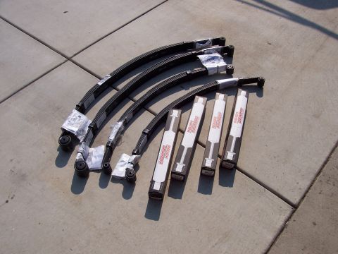 1970 Jeep Jeepster - Leaf springs and shock absorbers are laid out on a concrete surface, with 'ROUGH COUNTRY' visible on the packaging.