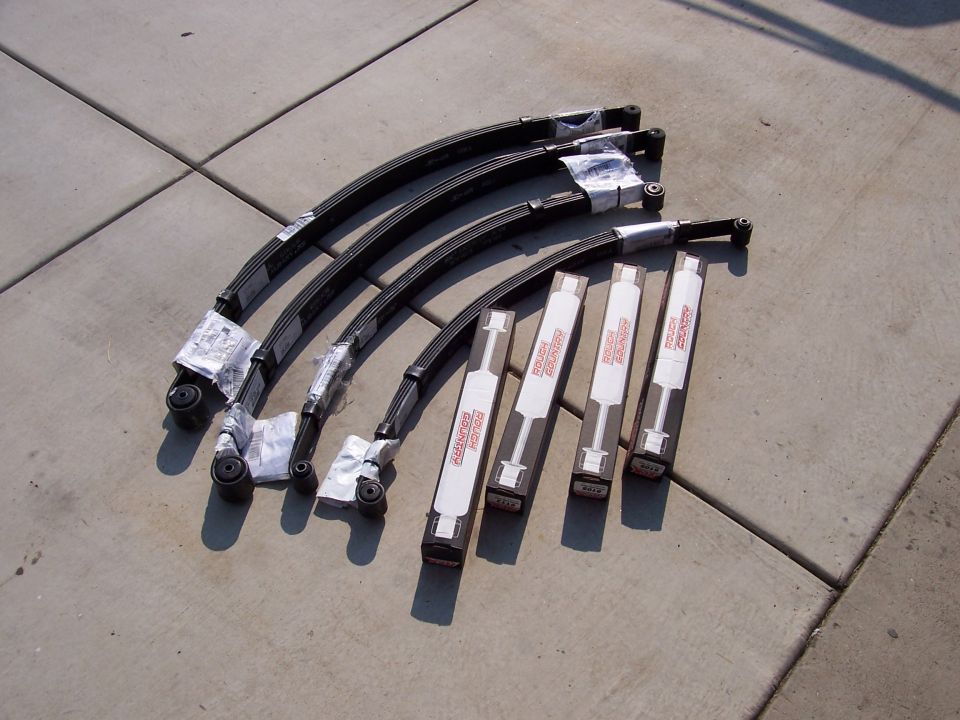 Four new leaf springs and four Rough Country shocks laid out on concrete