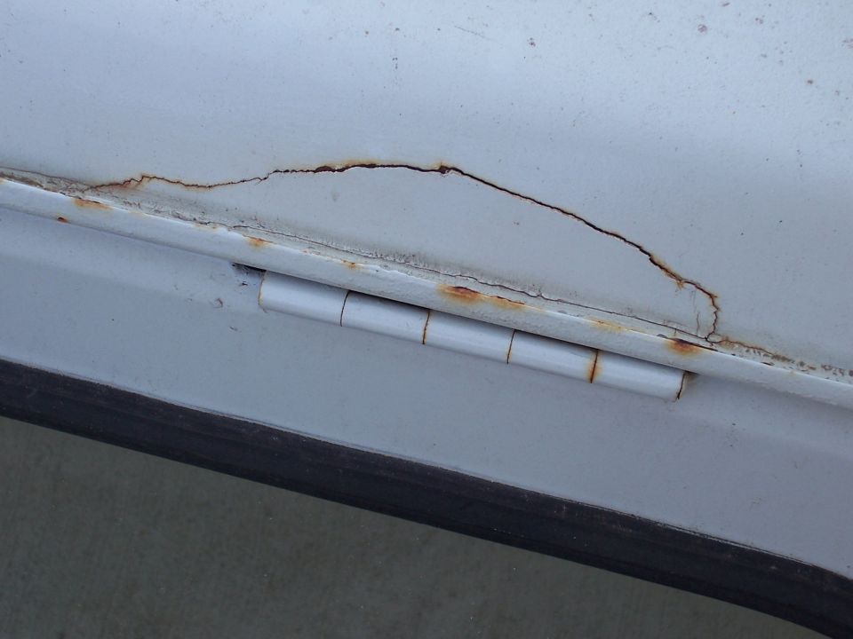 close-up of a white door hinge with rust and cracks in the paint