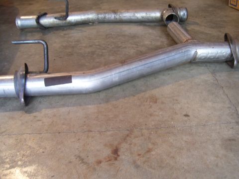 1990 Ford Mustang - Two exhaust pipes are shown on a concrete surface, likely for sale as parts.
