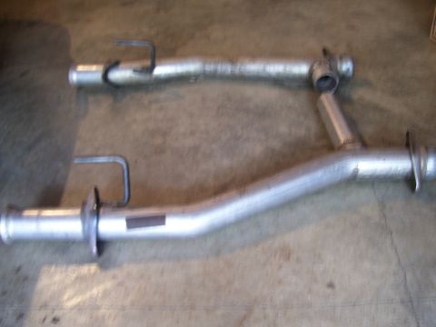 1990 Ford Mustang - Two exhaust pipes are shown on a concrete surface. One pipe is significantly cleaner than the other.