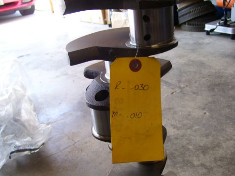 1990 Ford Mustang - A crankshaft is shown with a yellow tag indicating measurements, with a car visible in the background.