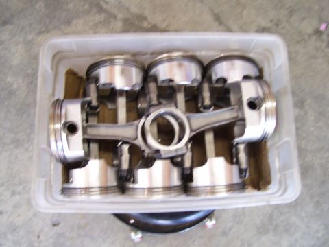 1990 Ford Mustang - A set of four pistons and connecting rods are organized in a clear plastic container.